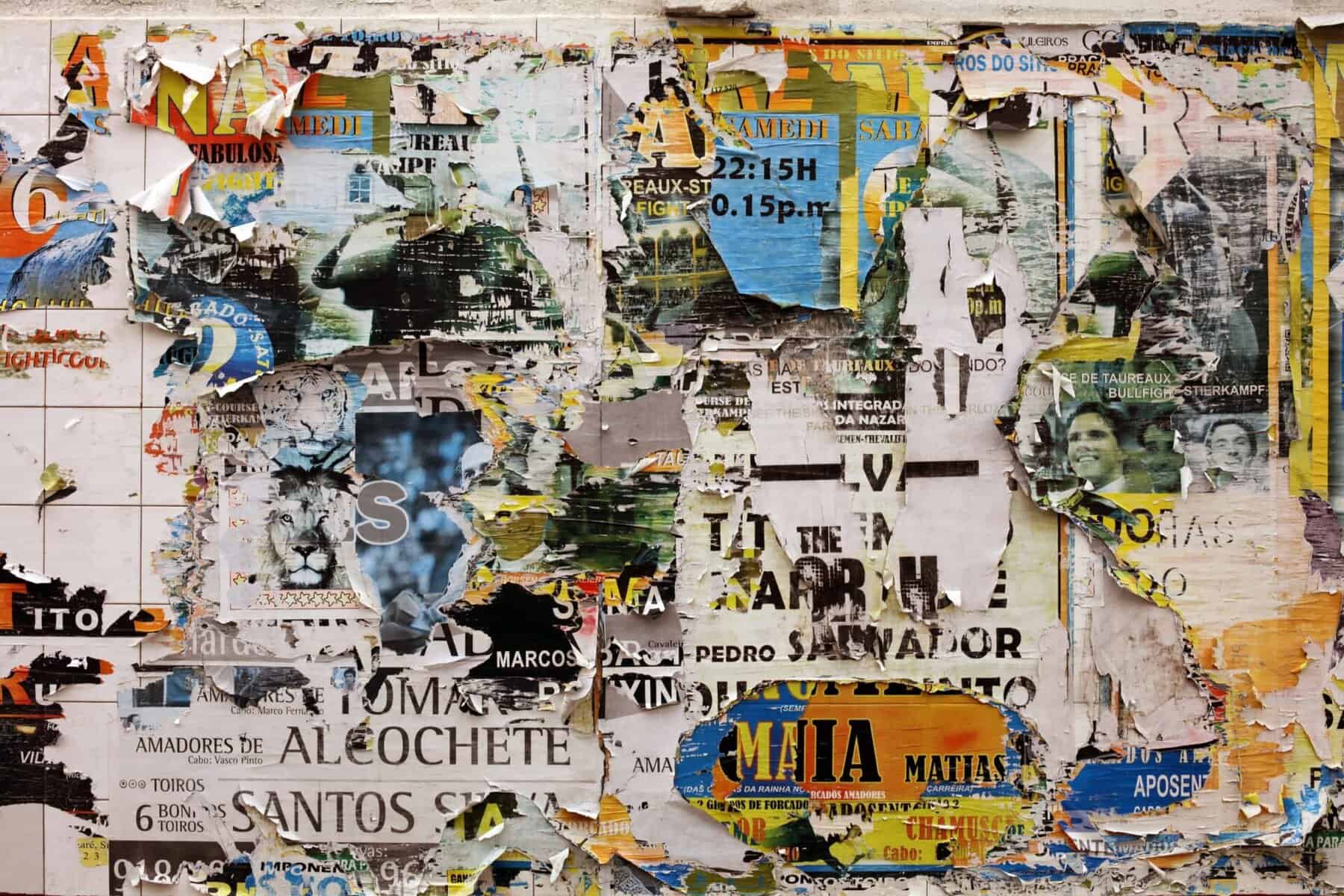 Vibrant, peeling posters on urban wall showcasing torn advertisements and flyers.